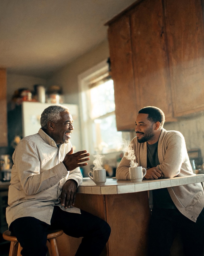 A son and his dad laughing together over morning coffee at the kitchen counter